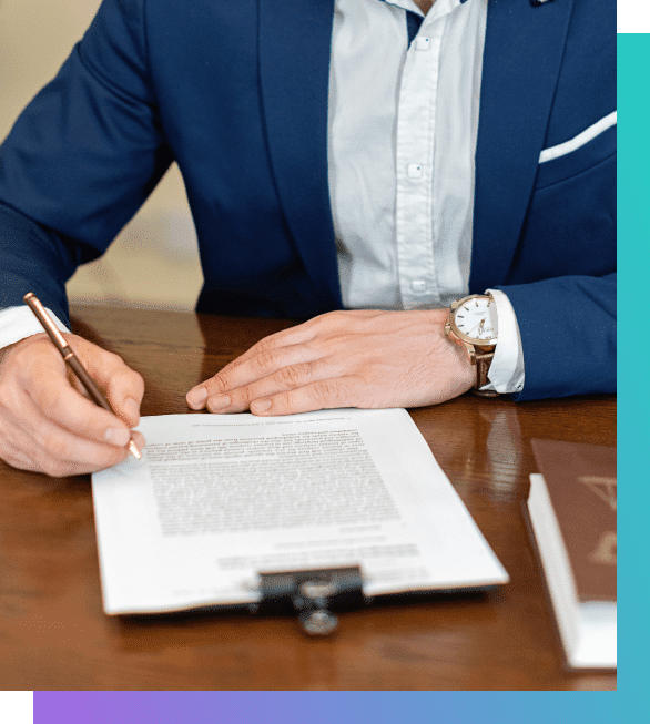 A person in a blue suit and white shirt with a gold watch signs a document with a pen.