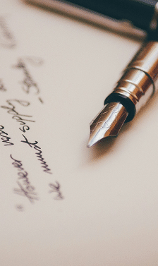 A silver fountain pen with a detailed nib rests on a piece of paper with handwritten cursive text.